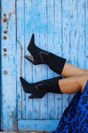 Botas de serraje en color negro. Acabado en punta. Detalle de tachuelas en la parte media de la bota. Caña caída. Altura tacón: 10 cm, suela 0,5 cm. Altura caña: 30 cm. 100% piel. Alabama Shop