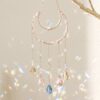 Elegante móvil <strong>de refracción solar </strong>de estilo celestial, fabricado con una cadena dorada y dijes de latón en forma de sol y luna creciente. Incluye prismas de cristal facetado de alta calidad que refractan la luz solar, creando destellos de arcoíris en cualquier habitación. Ideal para decoración bohemia o espacios de meditación. Alabama Shop