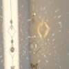 Elegante móvil <strong>de refracción solar </strong>de estilo celestial, fabricado con una cadena dorada y dijes de latón en forma de sol y luna creciente. Incluye prismas de cristal facetado de alta calidad que refractan la luz solar, creando destellos de arcoíris en cualquier habitación. Ideal para decoración bohemia o espacios de meditación. Alabama Shop